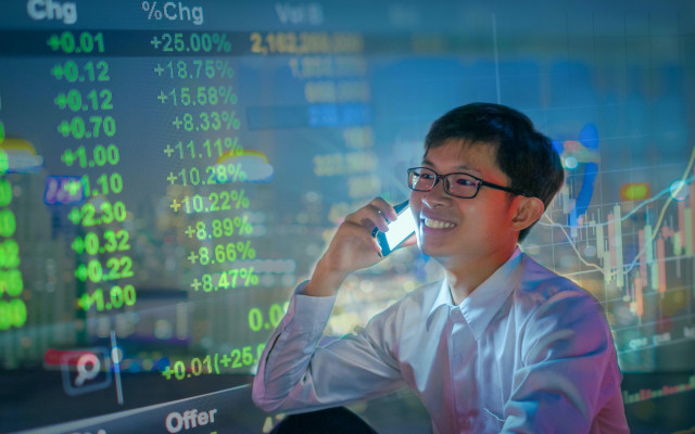 Slika mladega poslovnega moskega iz Kitajske ki uporablja pametni telefon za borzno analizo s hologramskim ozadjem borznih zelenih tecajev 28012023