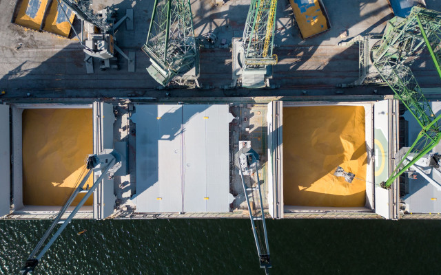 Slika pogleda iz zraka na ladjo za prevoz razsutega tovora natovorjeno z zitom ki je zasidrana v prometnem pristaniscu v ozadju pa so vidni delavci in stroji 20.1.2024