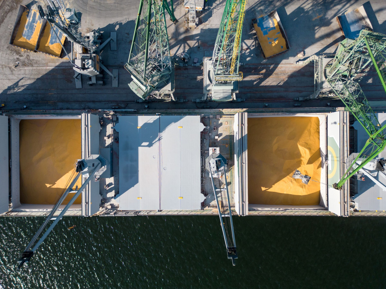 Slika pogleda iz zraka na ladjo za prevoz razsutega tovora natovorjeno z zitom ki je zasidrana v prometnem pristaniscu v ozadju pa so vidni delavci in stroji 20.1.2024