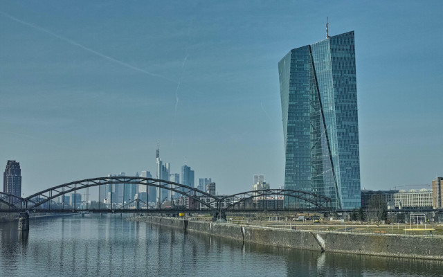 Slika stavbe evropske centralne banke v Frankfurtu z zeleznim mostom cez reko v ospredju 05032023