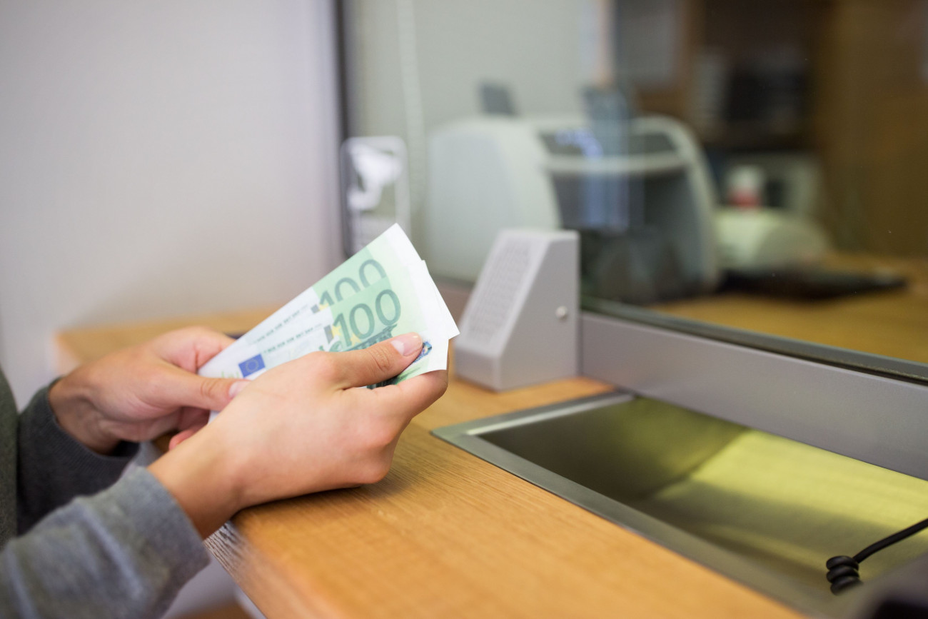 Slika zenskih rok blagajnicarke na banki ob stetju 100 evrskih bankovcev na bancnem okencu 13.2.2023