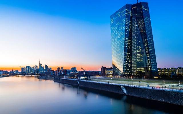 Slika zgradne evropske centralne banke in neboticnika v soncnem zahodu in recni kanal v ospredju 4.2.2024