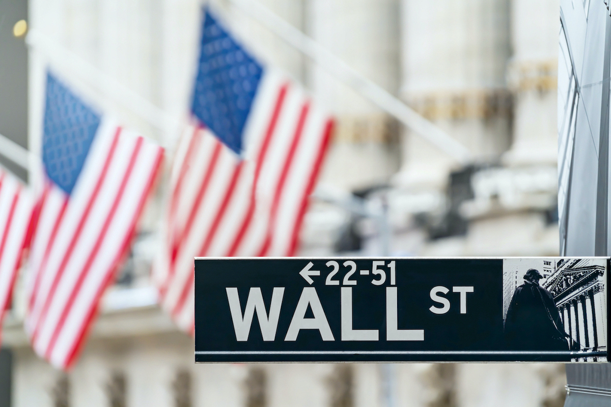 Slika znaka za Wall street v New Yorku ki kaze na financno ekonomsko in poslovno okrozje z ameriskimi zastavami na drogu v ozadju 07032023